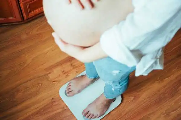 Image of woman weighing herself and experiencing weight gain through pregnancy Bellshill